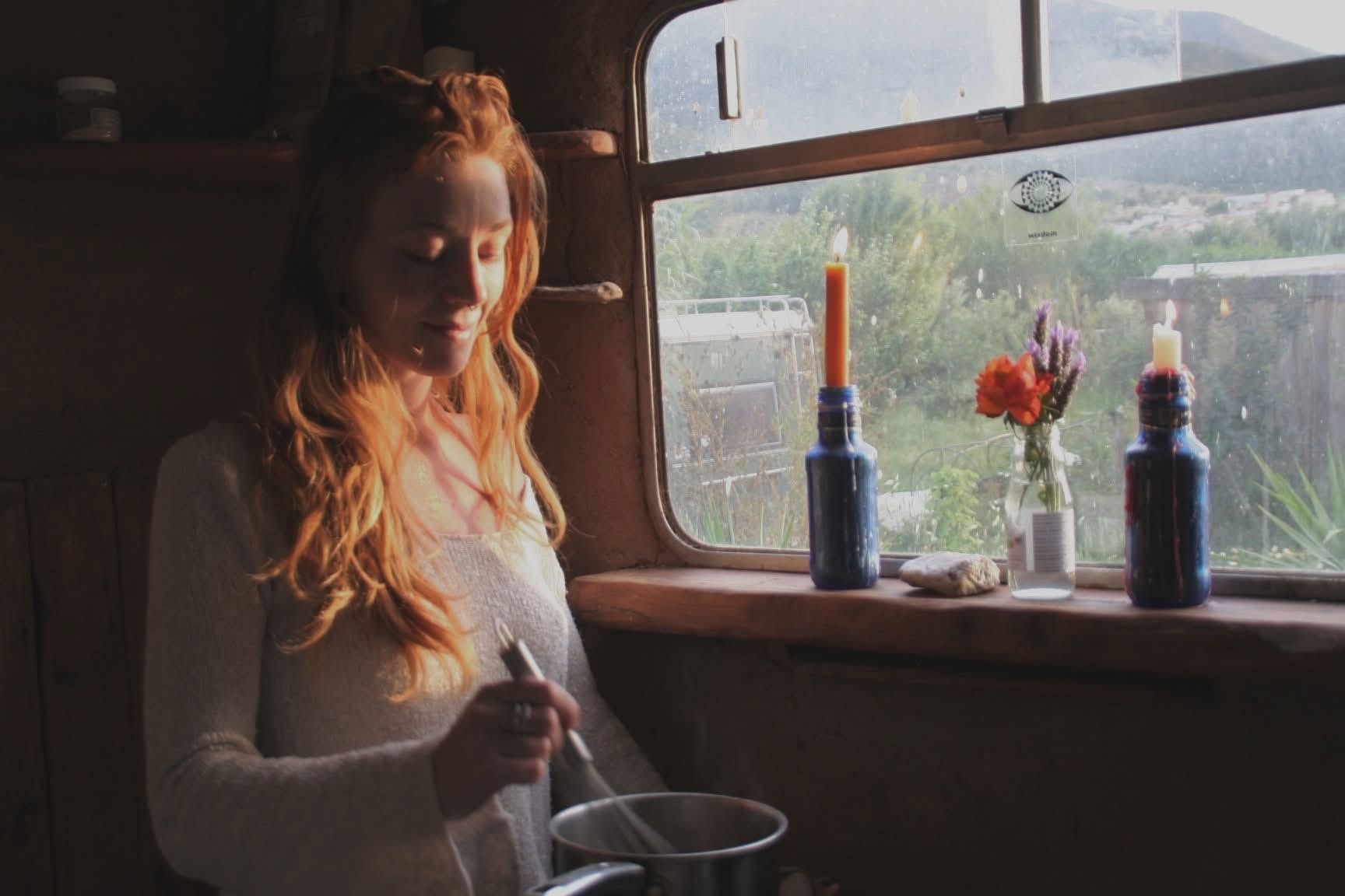 Eliza Fern stirring a pot beside a sunlit window with flowers and candles