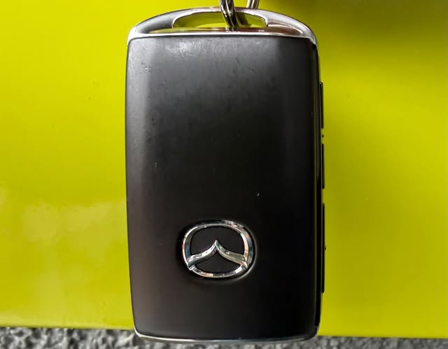 A black Mazda key fob photographed against a yellow background.