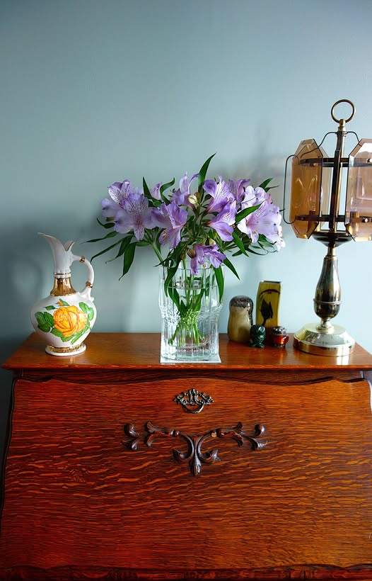 Purple and yellow flowers in a glass vase on an antique wooden cabinet