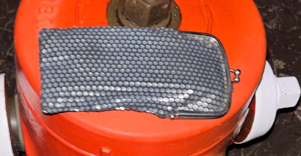 A small grey patterned case resting on an orange roadside traffic barrel